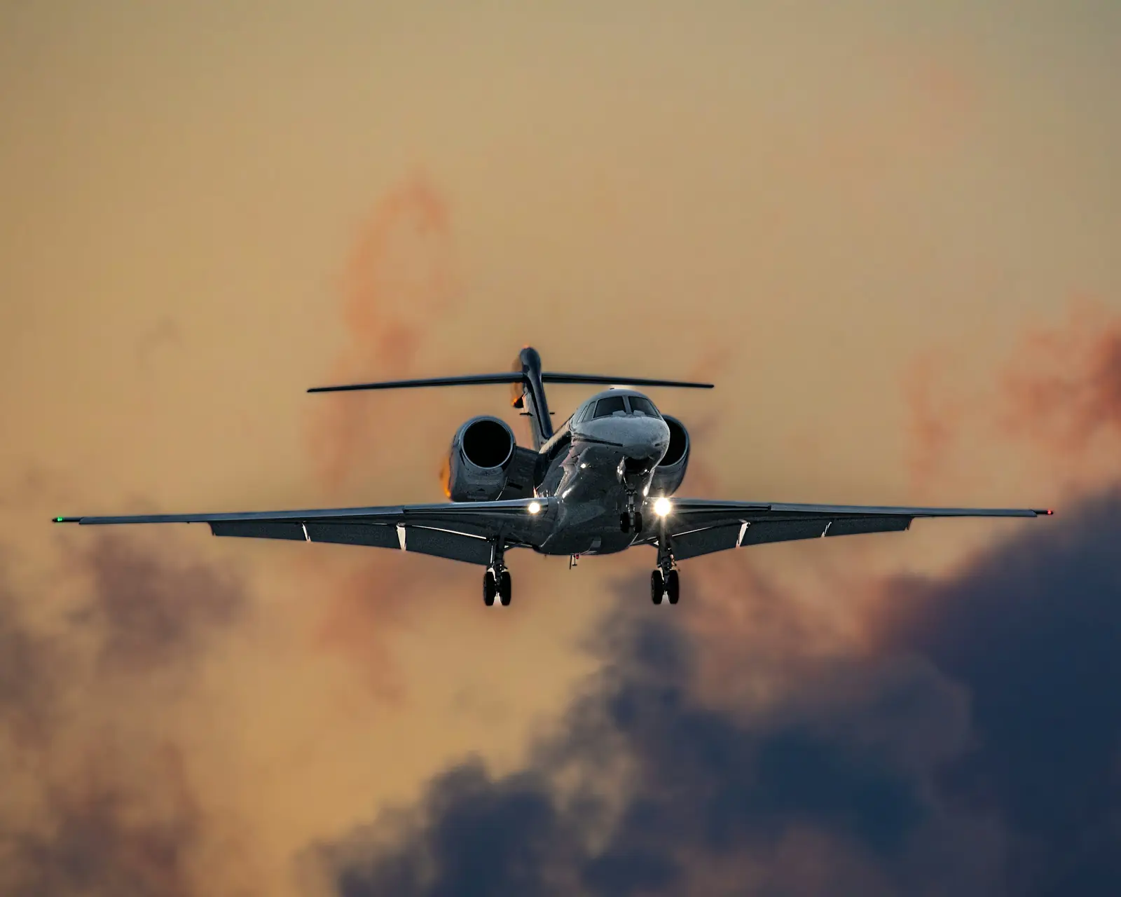 A business jet flying head-on through sunset clouds